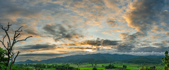 Beautiful view of morning light shining through clouds, mountains, green rice fields, trees and fog in rural Chiang Rai Province, Thailand.
