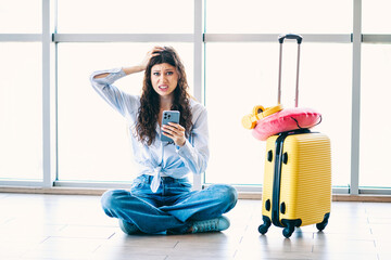 Charming Charming woman distressed while waiting in airport lobby with luggage and phone during...