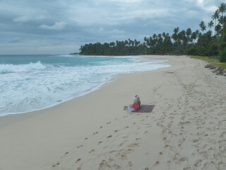 Aerial view of two friends enjoy the beauty of Indonesia's tropical beaches. Two young women sit together and chat on a beautiful tropical beach