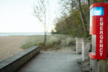 Emergency phone on a quiet beachside boardwalk near trees along Lake Michigan beachfront with copy space