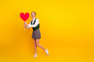 Young student holding a heart symbol on a vibrant yellow background, expressing happiness, joy, and...