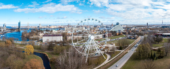 Large Ferris wheel in a park by a river, with bridges, a triangular glass building, a tall television tower, and mixed urban architecture visible.