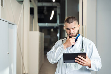 Young male healthcare professional in lab coat using digital tablet in clinical environment....