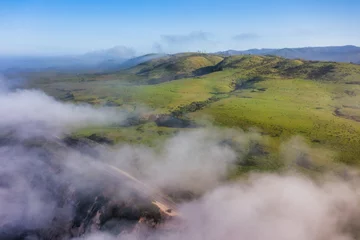 Fototapete Rund Aerial view of mist rolling over lush green hills along Highway 1 near Scott Creek Beach in California. Early morning fog adds a sense of mystery and serenity to the coastal landscape © Volodymyr