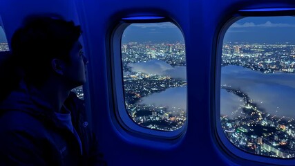 Asian man on airplane looking out window at illuminated city lights over cloud covered landscape at night footage. - Powered by Adobe