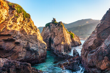 Narrow ocean channel surrounded by rugged cliffs at Garrapata State Park Bluff Trail along Highway 1, California. Warm sunset light highlights the rocky textures and dramatic landscape