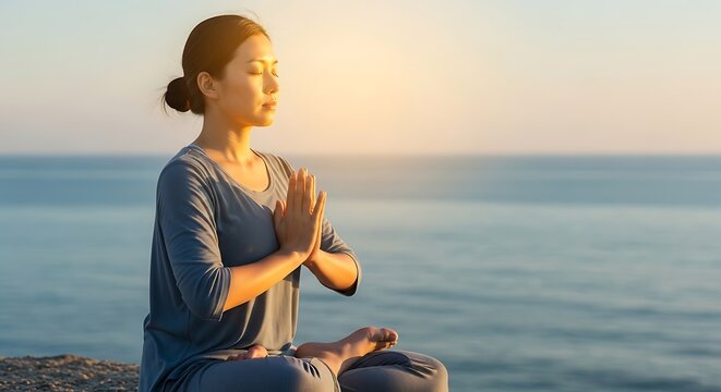 Asian woman meditating in lotus position by the ocean at sunrise.