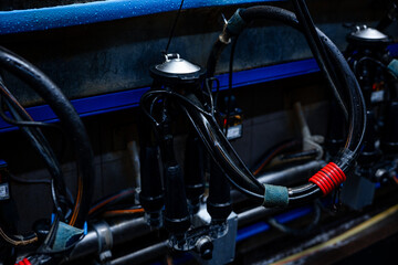 Milking machine setup with black rubber hoses, metal parts, blue piping, and a red band on a hose against a dark industrial backdrop.