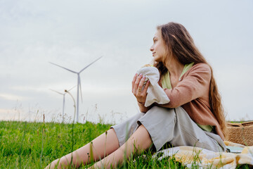 Woman relaxing with sandwich while gazing at wind turbines