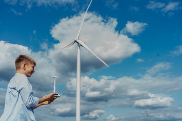 Teenage boy holding wind turbine model in field with real turbines behind