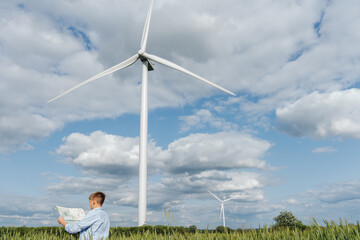 Teenage boy reading map in field with large wind turbine in background