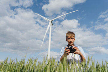 Teen boy using camera in wheat field with wind turbine behind him