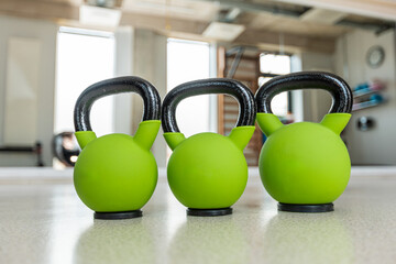 Three vibrant green kettlebells with black handles are aligned on a polished surface in a gym....