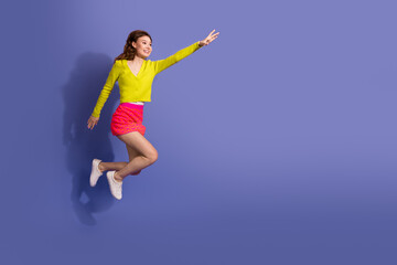 Obraz premium Joyful young woman in trendy attire leaping against a vibrant purple background showcasing fashion and happiness