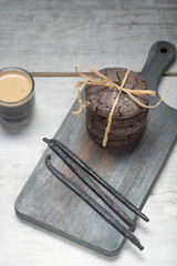 Close up studio still life photo with soft light and muted colors featuring dried vanilla beans on a vintage wooden board  with espresso and cookies in the background