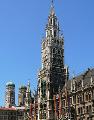 the gothic tower of the new City Hall in Munich decorated with the LGBT flags in June 2025, in background the twin bell towers of the Frauenkirche