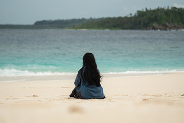 A young woman enjoys the beauty of a tropical beach. A young woman sits alone on the beach