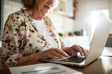 Senior woman managing finances online at home kitchen table