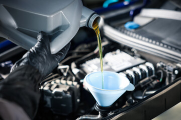 Worker pouring motor oil from canister into car engine, closeup