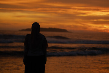 Fototapeta premium A woman enjoys the view of the beach at sunset