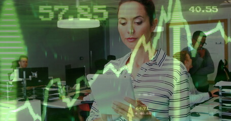 Examining striped blouse woman reviewing graphs on tablet in office, with monitors and lights
