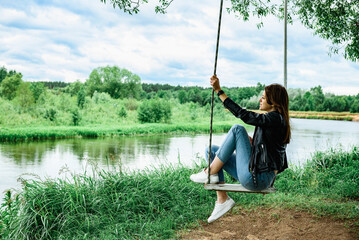 A happy young girl is sitting on a swing in a beautiful tree by the river.
