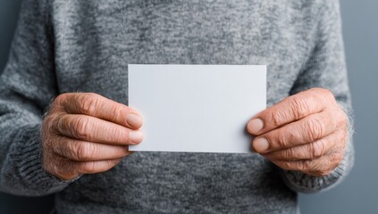 Senior man in sweater holding blank card with copy space on grey background