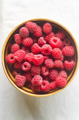Ripe pink raspberries in a ceramic bowl on a white background. Summer berry harvest concept. Vertical orientation. Selective focus. Top view