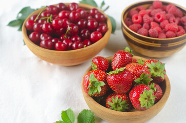 Three types of berries in ceramic bowls on a white background. Strawberries, cherries and raspberries. Summer berry harvest concept. Horizontal orientation. Selective focus.
