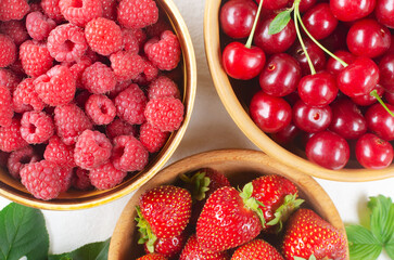 Three types of berries in ceramic bowls on a white background. Strawberries, cherries and raspberries. Summer berry harvest concept. Horizontal orientation. Selective focus. Top view