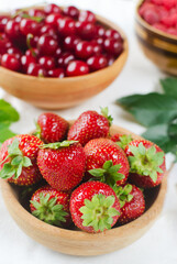 Three types of berries in ceramic bowls on a white background. Strawberries, cherries and raspberries. Summer berry harvest concept. Vertical orientation. Selective focus.