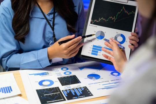 Businesswomen pointing at charts and graphs, discussing blockchain and stock investment opportunities during a meeting