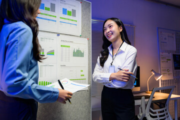 Two Asian businesswomen reviewing positive data about company performance, smiling and discussing...