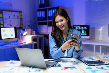 Young business woman using smartphone and working with financial documents in office at night