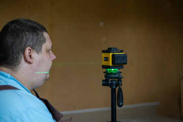 A man takes measurements and aligns using a laser level on a tripod. The green beam of the laser level provides precise horizontal alignment for interior construction and renovation work.