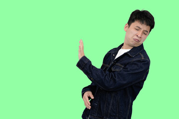 young asian man making rejection or dissaproval pose in green isolated background