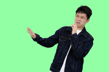 young asian man making rejection or dissaproval pose in green isolated background