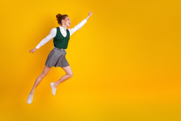 Energetic teenager jumps confidently against a vivid yellow background while expressing academic...
