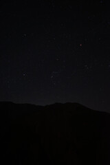 Fototapeta premium 埼玉県秩父市の山の稜線と冬の星空を捉えた風景。澄んだ空に輝くオリオン座が印象的で、静寂な自然美を感じる一枚。星空観察、天体、自然風景、旅行のイメージに最適な写真素材です。