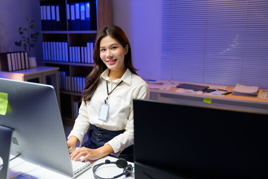 Asian businesswoman wearing shirt and lanyard working overtime using computer in office at night