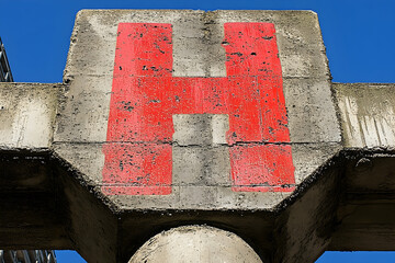 Weathered Concrete Structure with Bold Red "H" Against a Bright