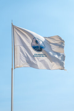 White flag with the logo of magdalena del mar municipality waving in the wind against a clear blue sky