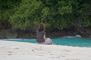 A young woman enjoys the beauty of a tropical beach. A young woman sits alone on the beach