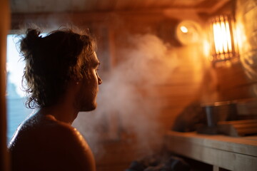 Fototapeta premium A man sitting on a wooden bench inside a hot traditional sauna, beads of sweat visible on their forehead and shoulders from the heat, with soft steam rising around them.