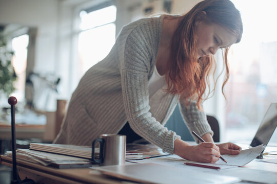 Focused female architect drawing plans at creative workspace desk