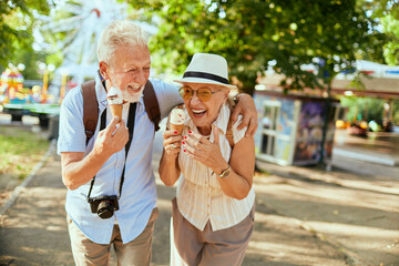 Senior couple laughing and eating ice cream at amusement park