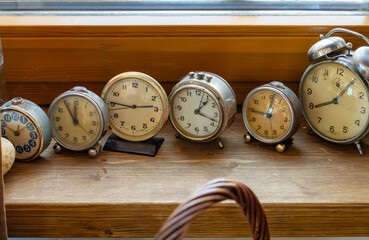 row of vintage alarm clocks placed on a wooden windowsill. Close-up of old-fashioned analog...