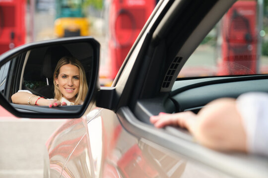 Businesswoman sitting in her electric vehicle adjusting rearview mirror at charging station - Powered by Adobe