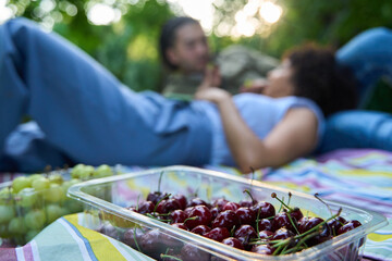 Close-up of cherries and grapes ready to be eaten by a couple relaxing in the background out of...