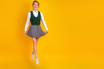 Youthful girl in stylish uniform smiling and jumping with joy against a vibrant yellow background